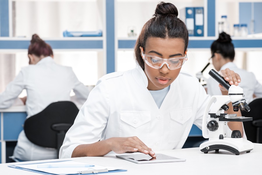 mulheres em laboratório usando microscópio para representar uma aula prática no sistema de educação híbrida