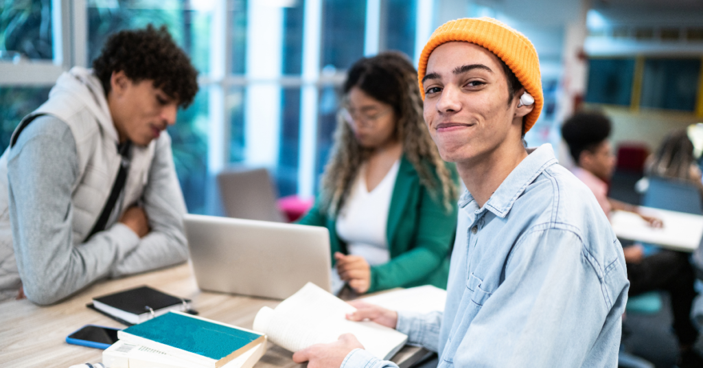 Um estudante de pele negra em uma sala de aula, aprendendo a como estudar para o vestibular de uma forma saudável, enquanto sorri para a câmera